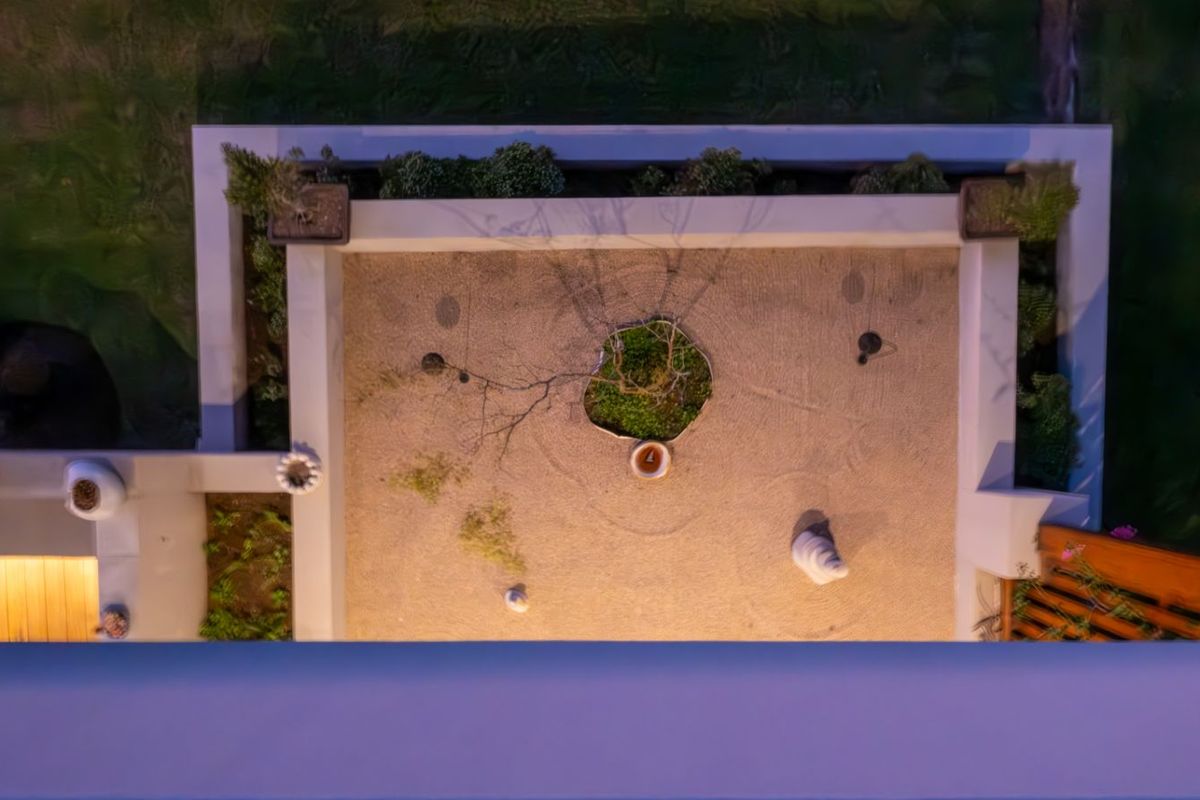 An overhead aerial view of a landscaped courtyard garden featuring a central tree, gravel ground cover, and perimeter retaining walls at night.