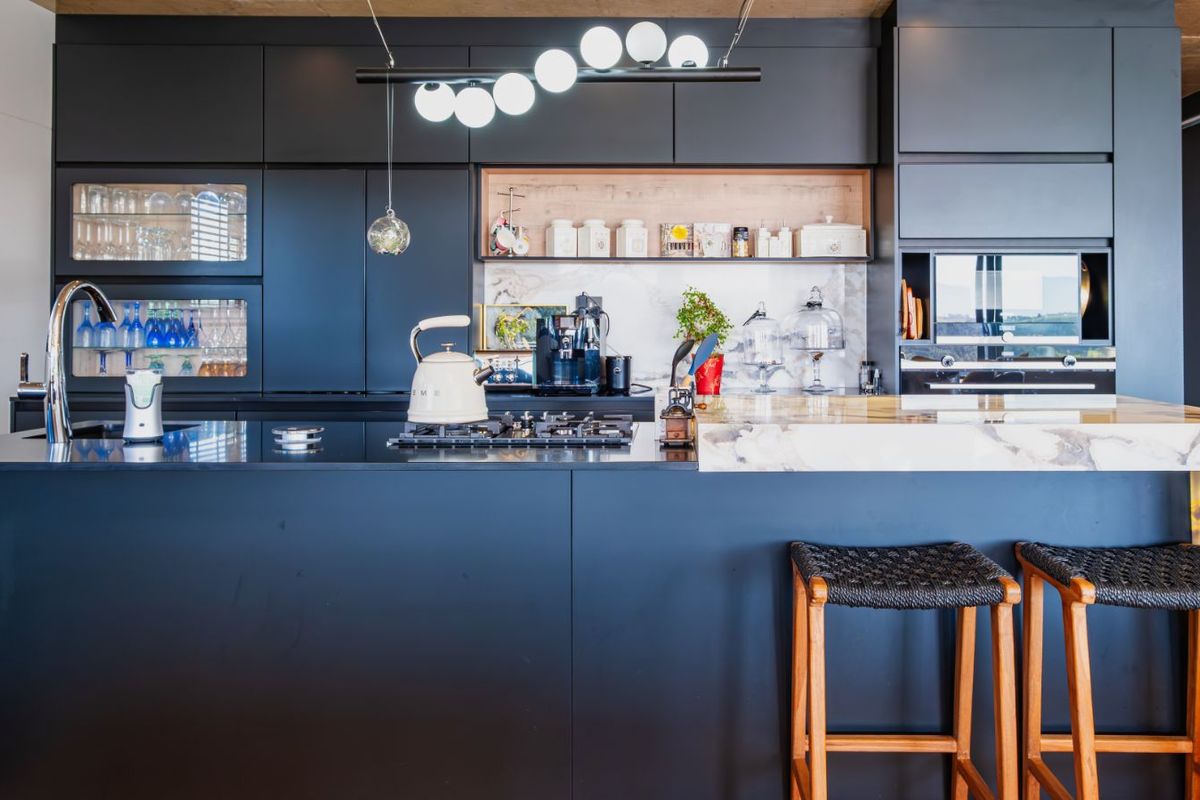 Modern kitchen featuring sleek matte black cabinetry, integrated appliances, a marble-topped island, and contemporary pendant lighting.