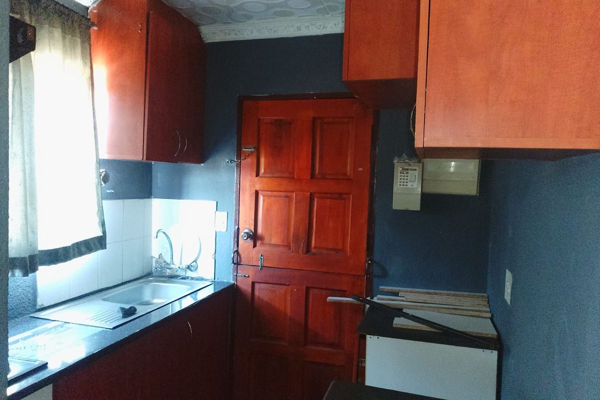 A compact kitchen featuring wooden cabinetry, a stainless steel sink, and a solid timber door, requiring cosmetic updates to modernize the space.