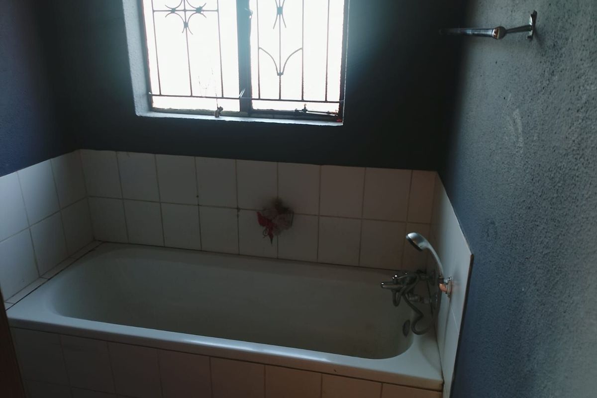 A bathroom featuring a built-in bathtub with tiled surround, a window with security bars, and a wall-mounted towel rail.