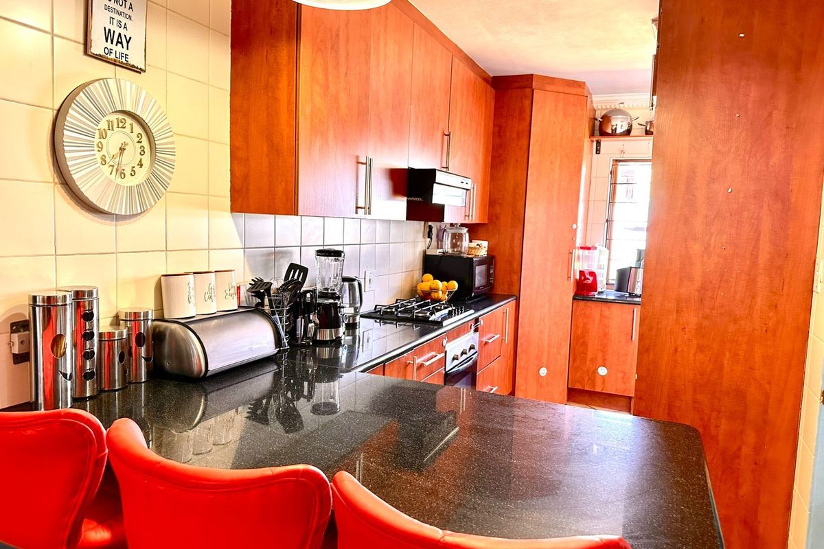 A functional kitchen featuring wood-finish cabinetry, dark granite countertops, a built-in gas hob, and an integrated oven, with a breakfast bar area.