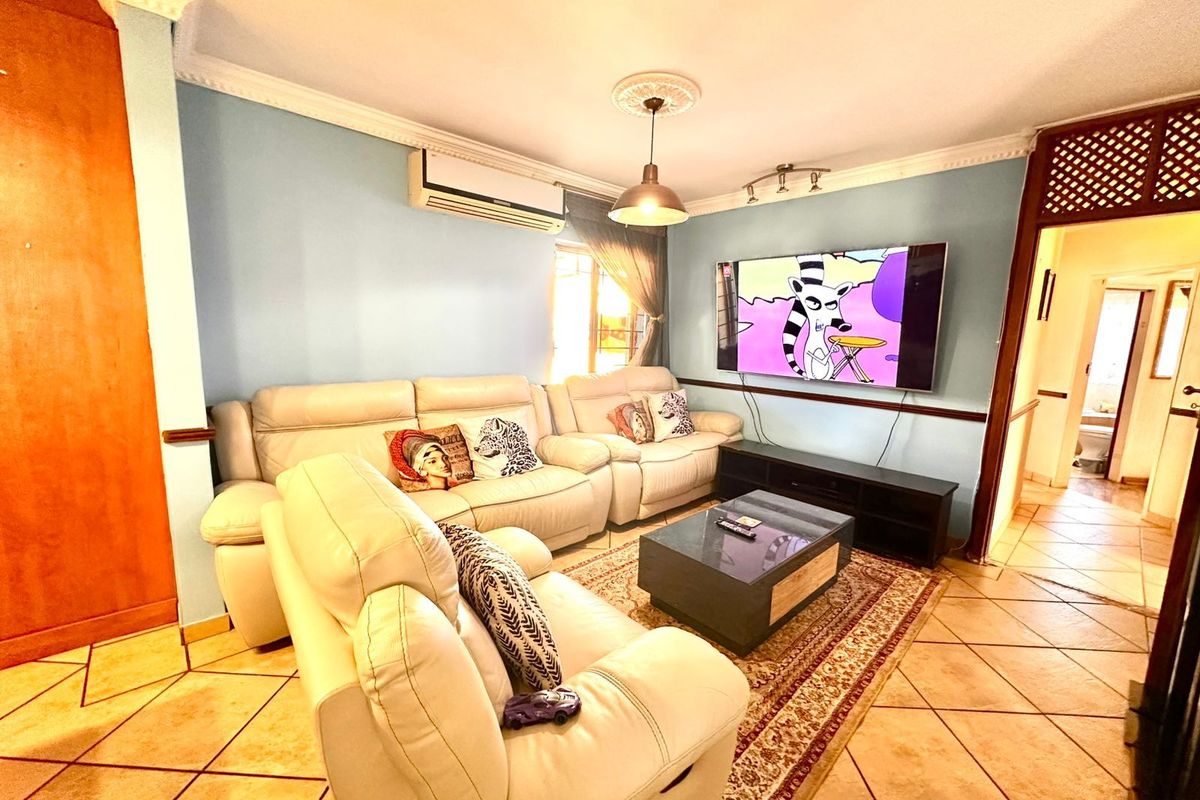 A comfortable living room featuring tiled flooring, crown molding, a ceiling rose, and a wall-mounted air conditioning unit.
