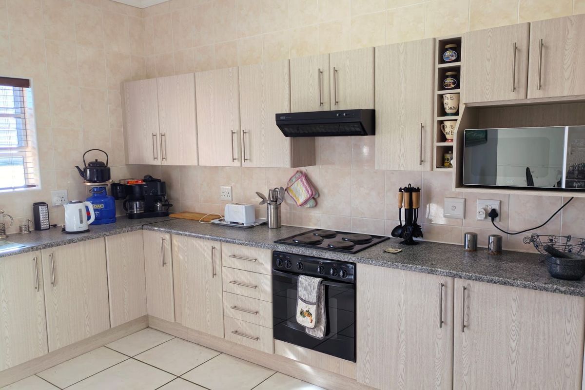 A functional kitchen featuring light wood-grain cabinetry, granite-look countertops, tiled splashbacks, a built-in oven, electric hob, and an integrated extractor fan.