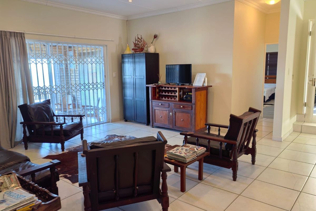 A spacious living area featuring tiled flooring, recessed ceiling lighting, and a sliding security gate leading to an outdoor patio space.