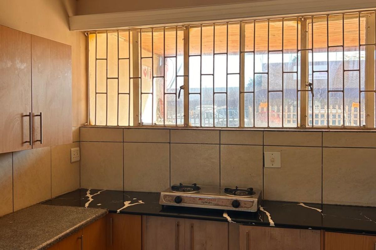A functional kitchen featuring wood-look cabinetry, black stone-effect countertops, a built-in gas hob, and tiled flooring with security bars on the window.