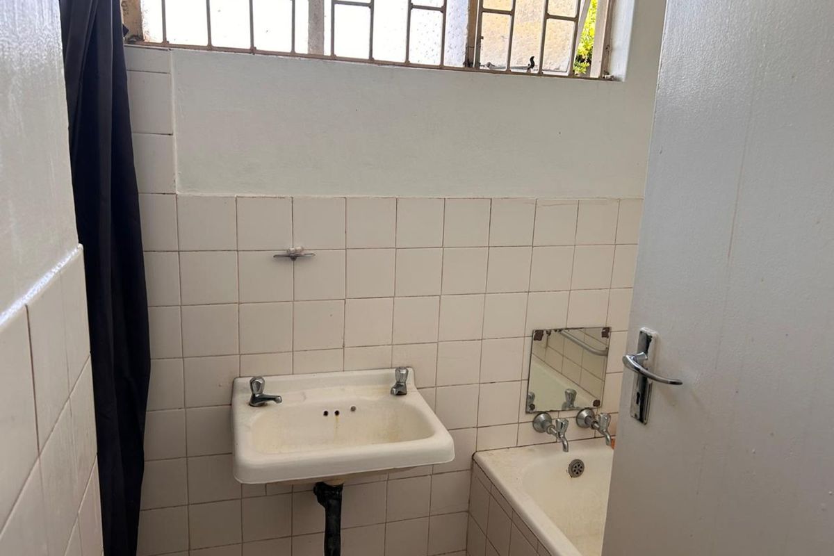 A compact bathroom featuring a wall-mounted basin, a bathtub, and tiled walls with security bars on the window.