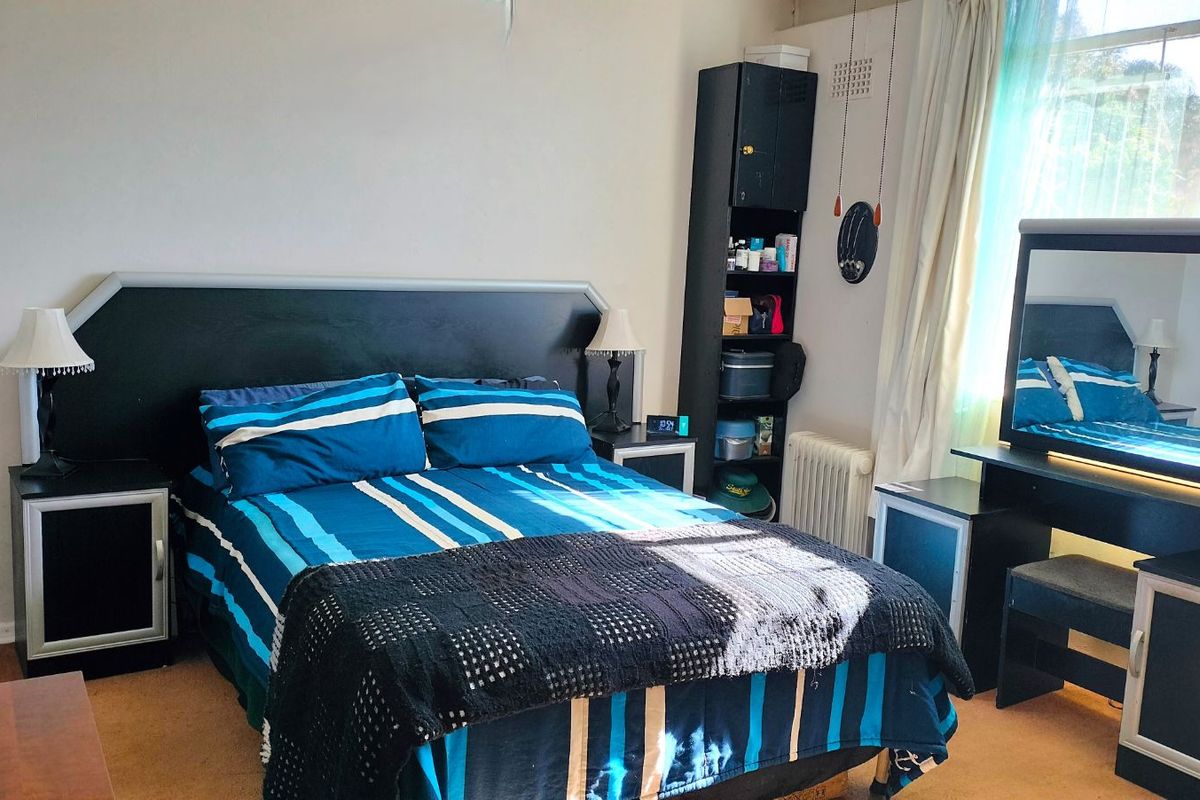A bedroom featuring a window with security bars and a radiator, providing a functional space with standard finishes.