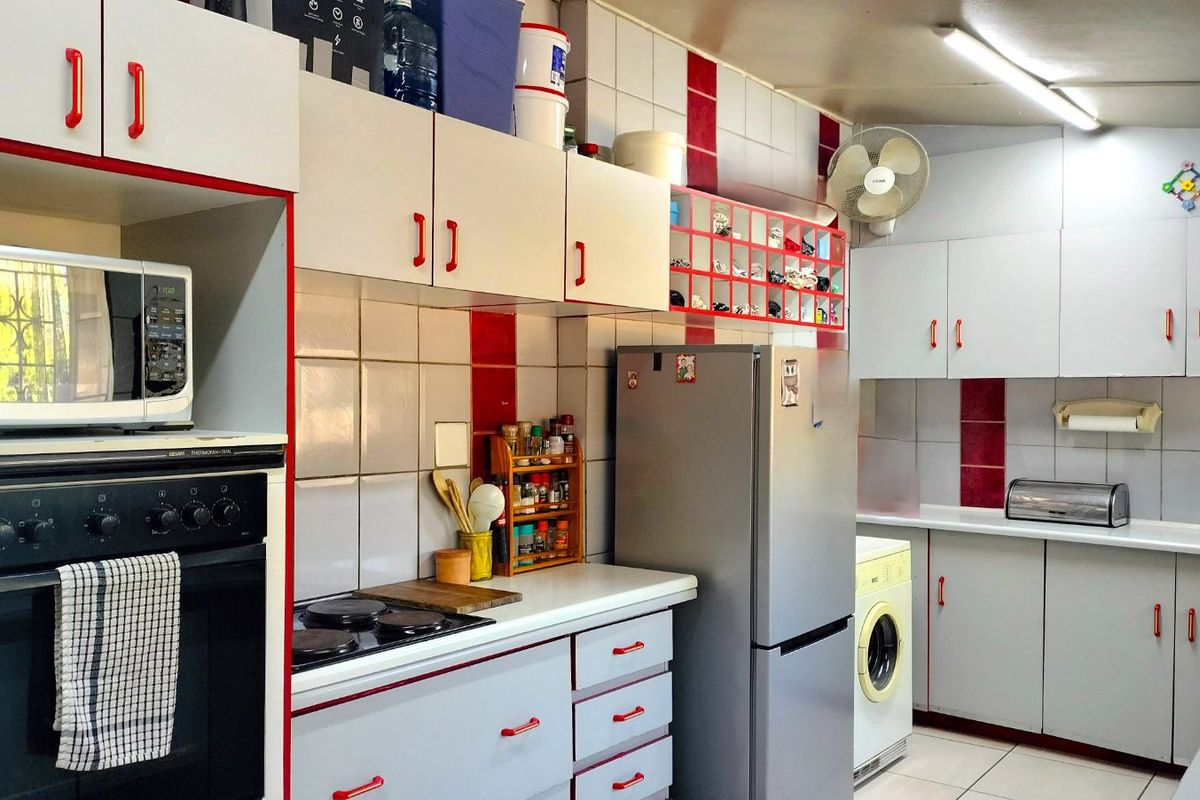 A functional kitchen featuring built-in cabinetry, tiled splashbacks, integrated oven, and hob, with dedicated space for laundry appliances.