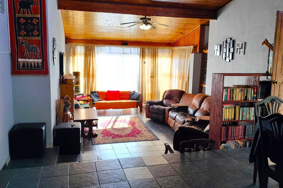 A spacious living area featuring a vaulted timber-clad ceiling, tiled flooring, and large windows that provide ample natural light.