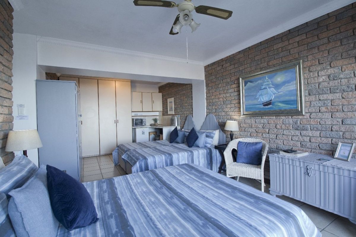Spacious bedroom featuring an exposed brick feature wall, built-in cupboards, and a small integrated kitchenette area with cabinetry.