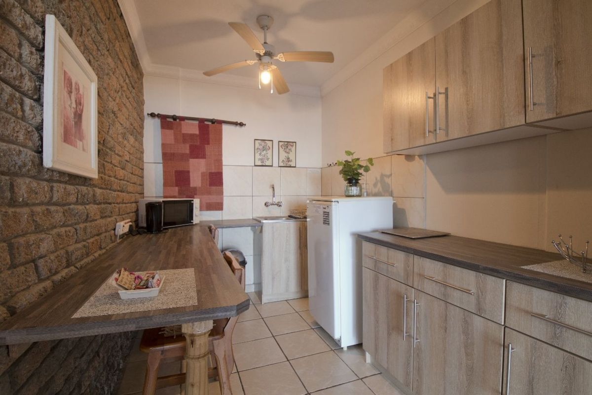 Compact kitchen featuring wood-look cabinetry, tiled splashbacks, a breakfast bar, and a distinctive exposed brick feature wall.