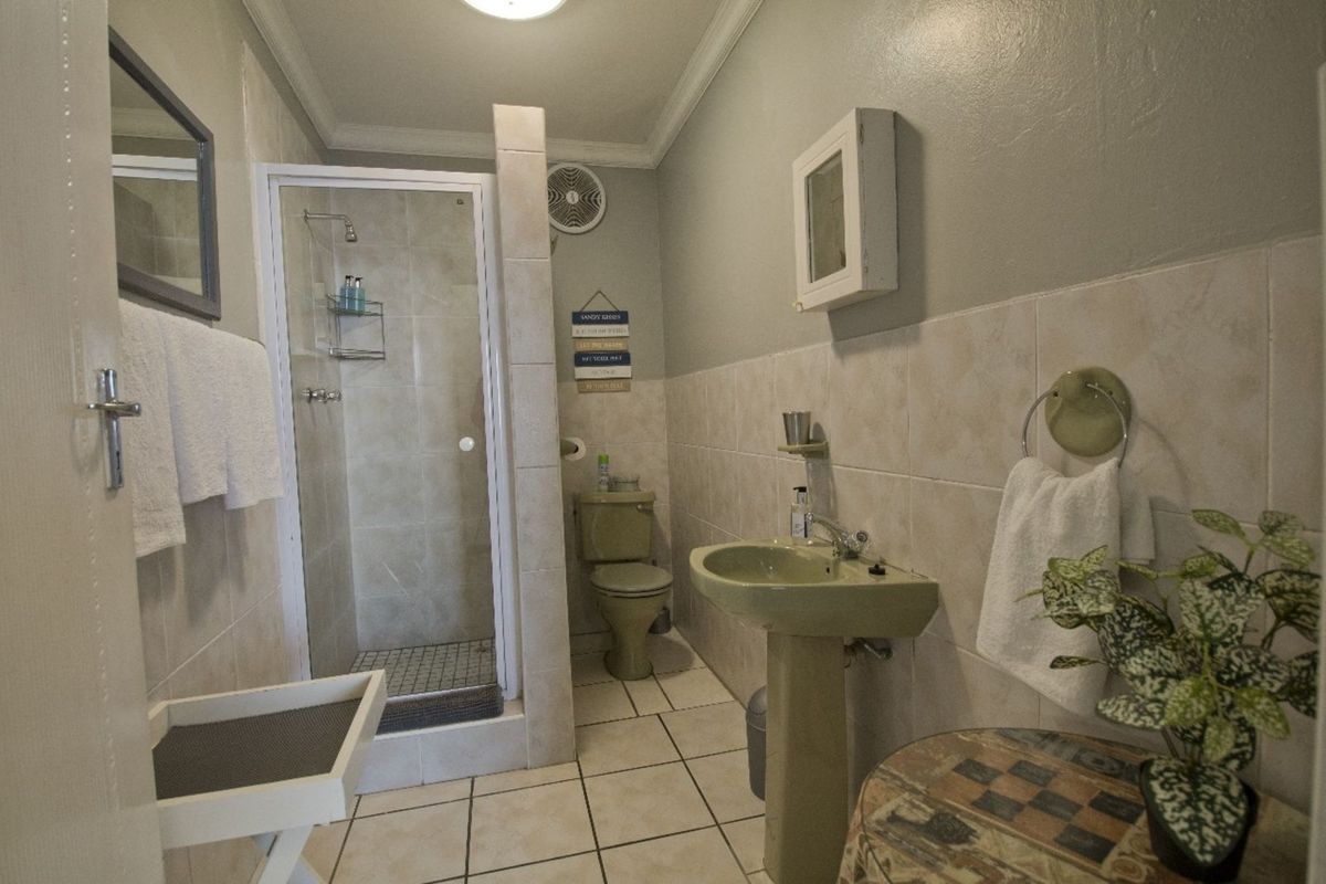 A functional bathroom featuring a glass-enclosed shower, pedestal basin, and toilet with neutral wall tiling and tiled flooring.