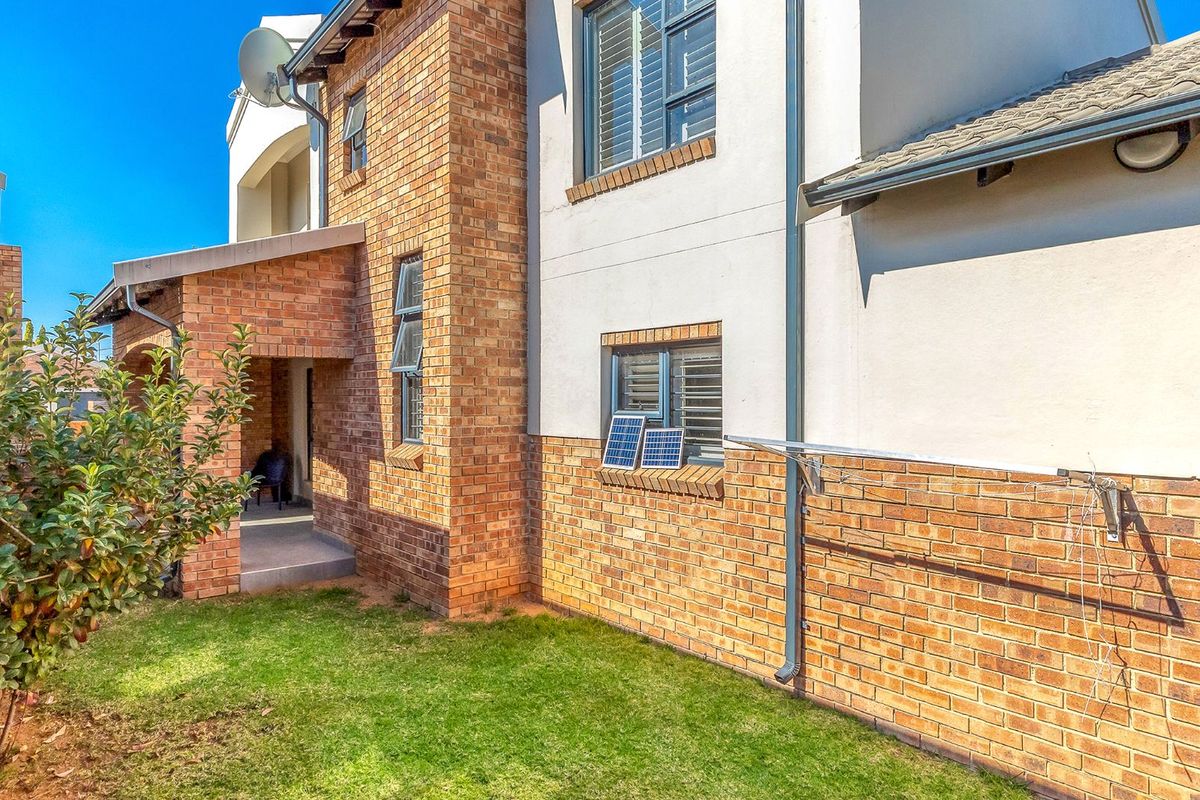 Rear view of the townhouse featuring a combination of face brick and plastered walls, aluminium window frames, and a small private garden area.