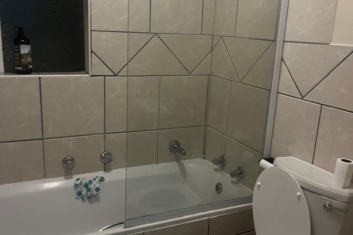 A functional bathroom featuring a bathtub with a glass shower screen, wall-mounted shower head, and a standard toilet.