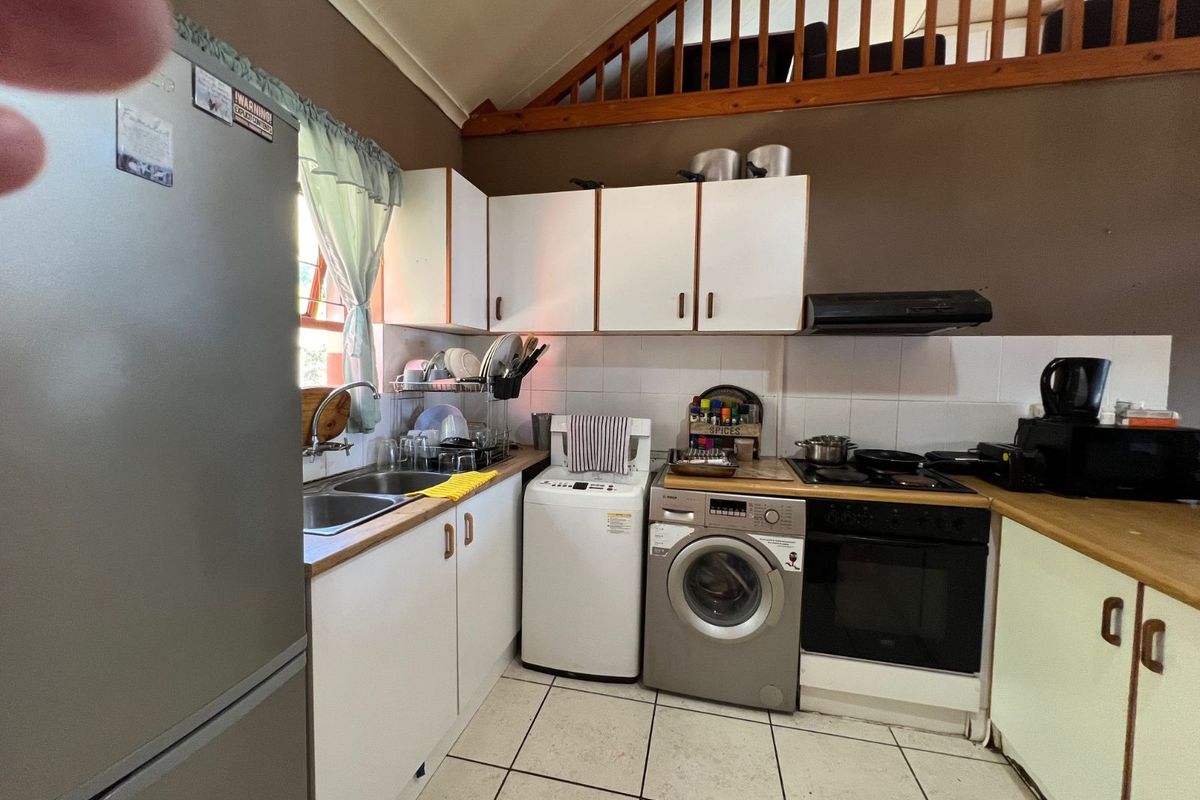 Compact kitchen featuring white cabinetry, integrated oven and hob, extractor fan, double sink, and dedicated space for laundry appliances under the counter.