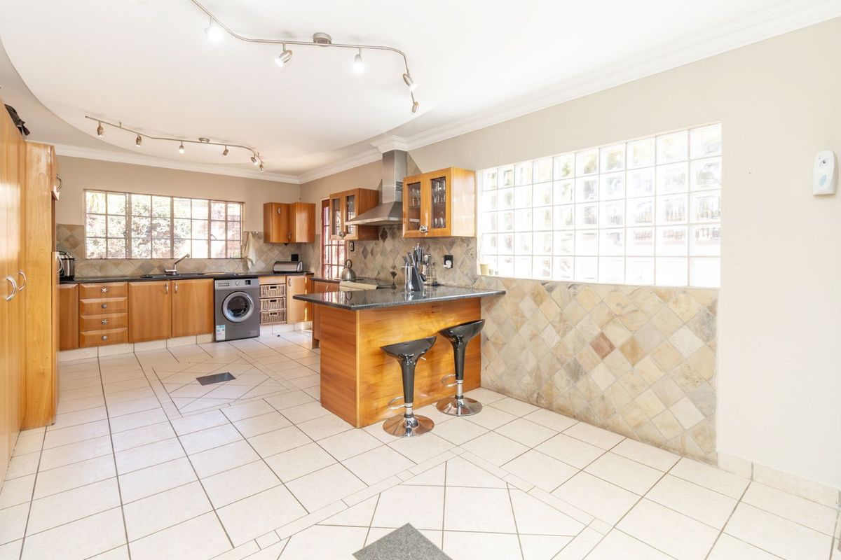 Spacious kitchen featuring wooden cabinetry, granite countertops, a central breakfast island, glass block feature wall, and tiled flooring throughout.