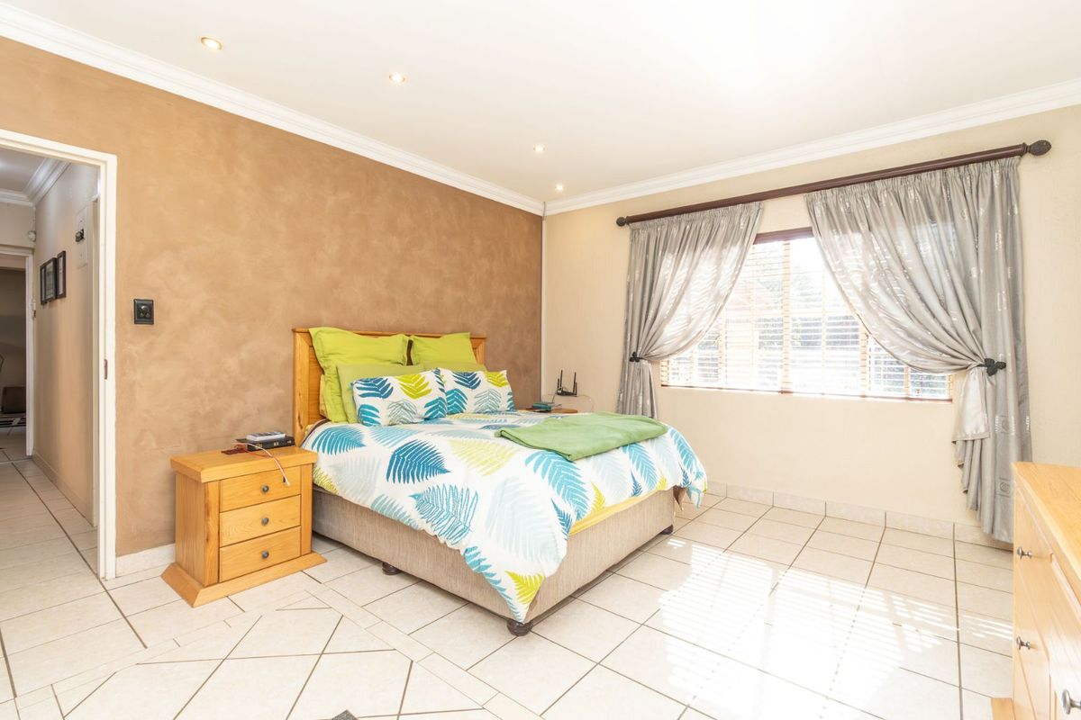 A well-lit bedroom featuring tiled flooring, recessed ceiling lighting, and a feature wall, providing a comfortable and functional living space.
