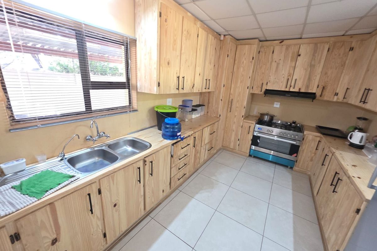 A functional kitchen featuring light wood cabinetry, a double stainless steel sink, tiled flooring, and a built-in gas stove with an extractor fan.