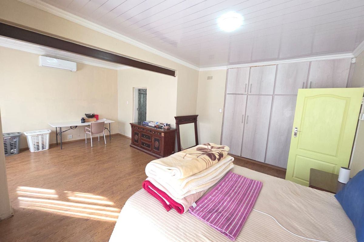 Spacious bedroom featuring built-in cupboards, laminate flooring, and a wall-mounted air conditioning unit.
