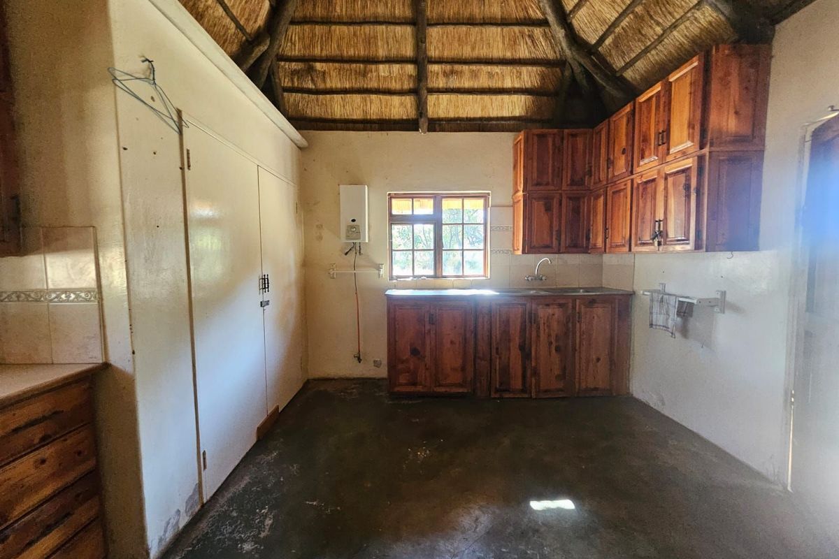 Rustic kitchen area featuring a traditional thatched roof, wooden cabinetry, and concrete flooring, offering a unique farm-style aesthetic with potential for modernization.