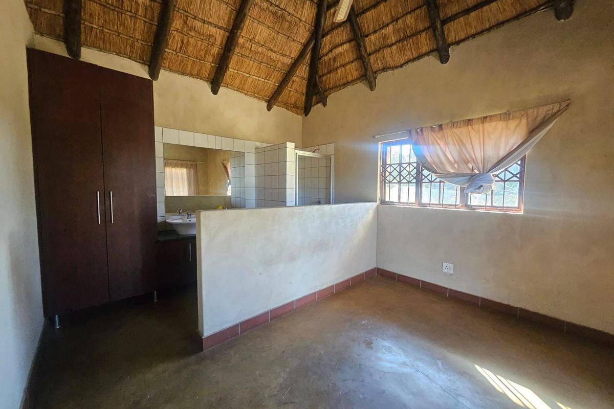 A rustic bedroom featuring a traditional thatched roof, built-in cabinetry, and an open-plan en-suite bathroom area with a vanity and shower.