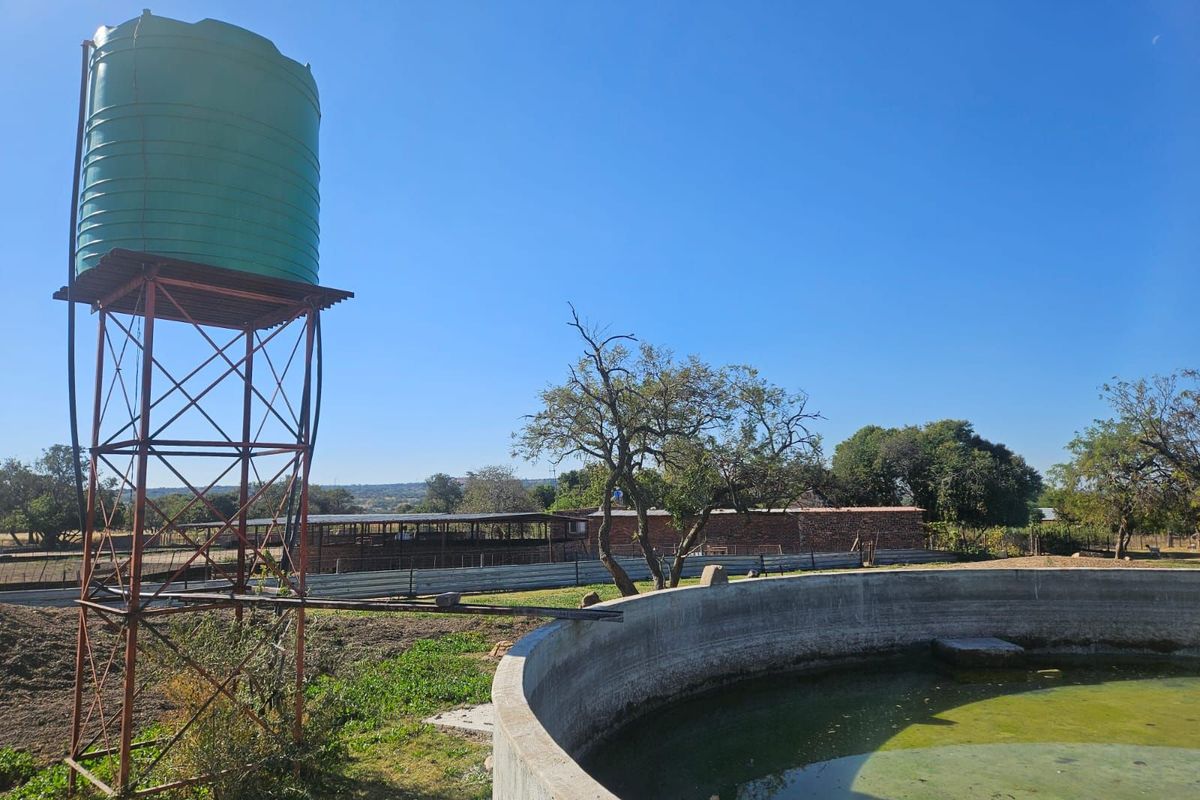 Farm infrastructure featuring a raised water storage tank and a concrete circular reservoir, set within an open agricultural landscape.