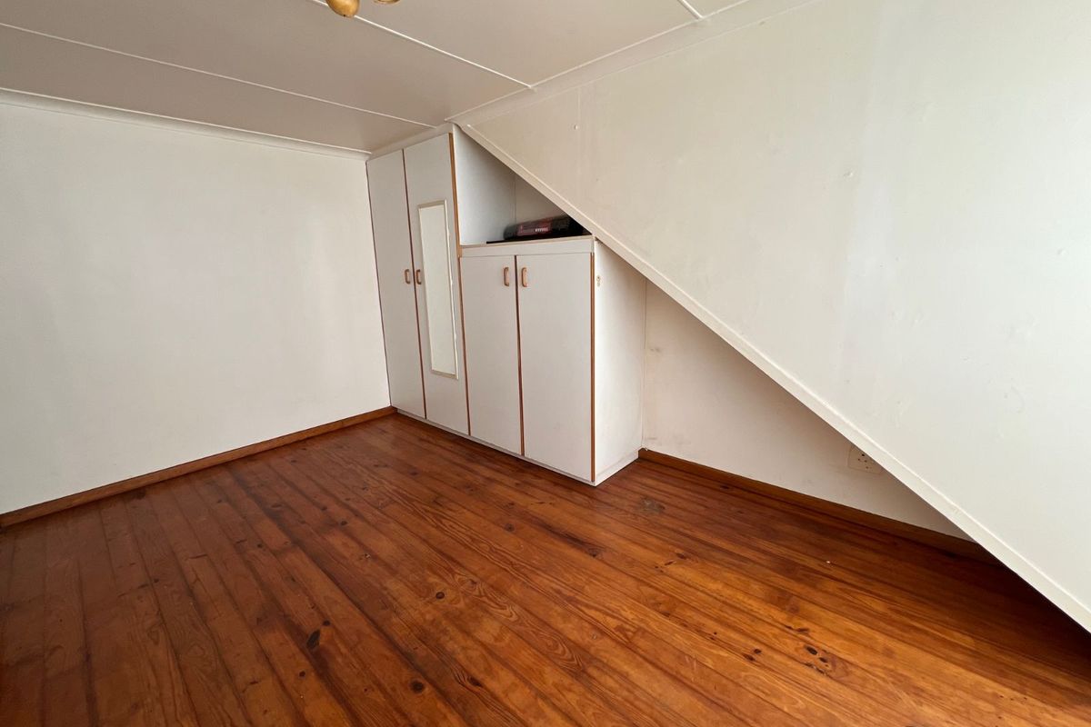 An empty bedroom featuring timber flooring, built-in cupboards, and a sloped ceiling design.