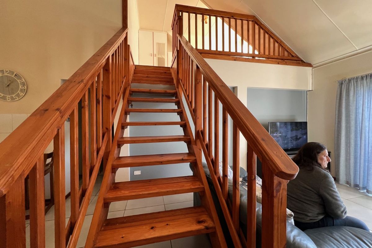 Living area featuring a prominent wooden staircase with balustrade, tiled flooring, and a vaulted ceiling, creating an open and airy atmosphere.