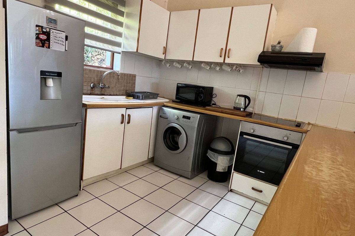 A functional kitchen featuring white cabinetry, tiled backsplash, built-in oven with hob, extractor fan, and tiled flooring.