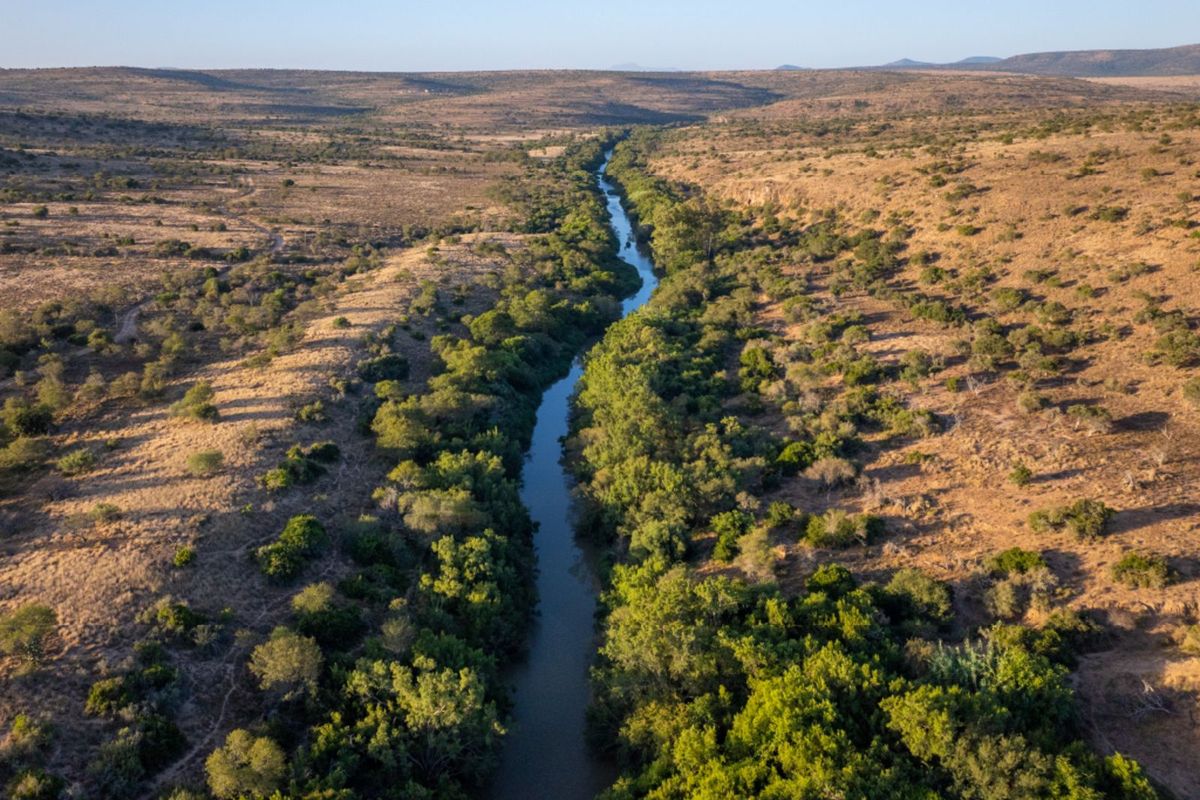 An aerial view of the farm landscape featuring a natural river winding through the valley, surrounded by indigenous vegetation and open terrain.