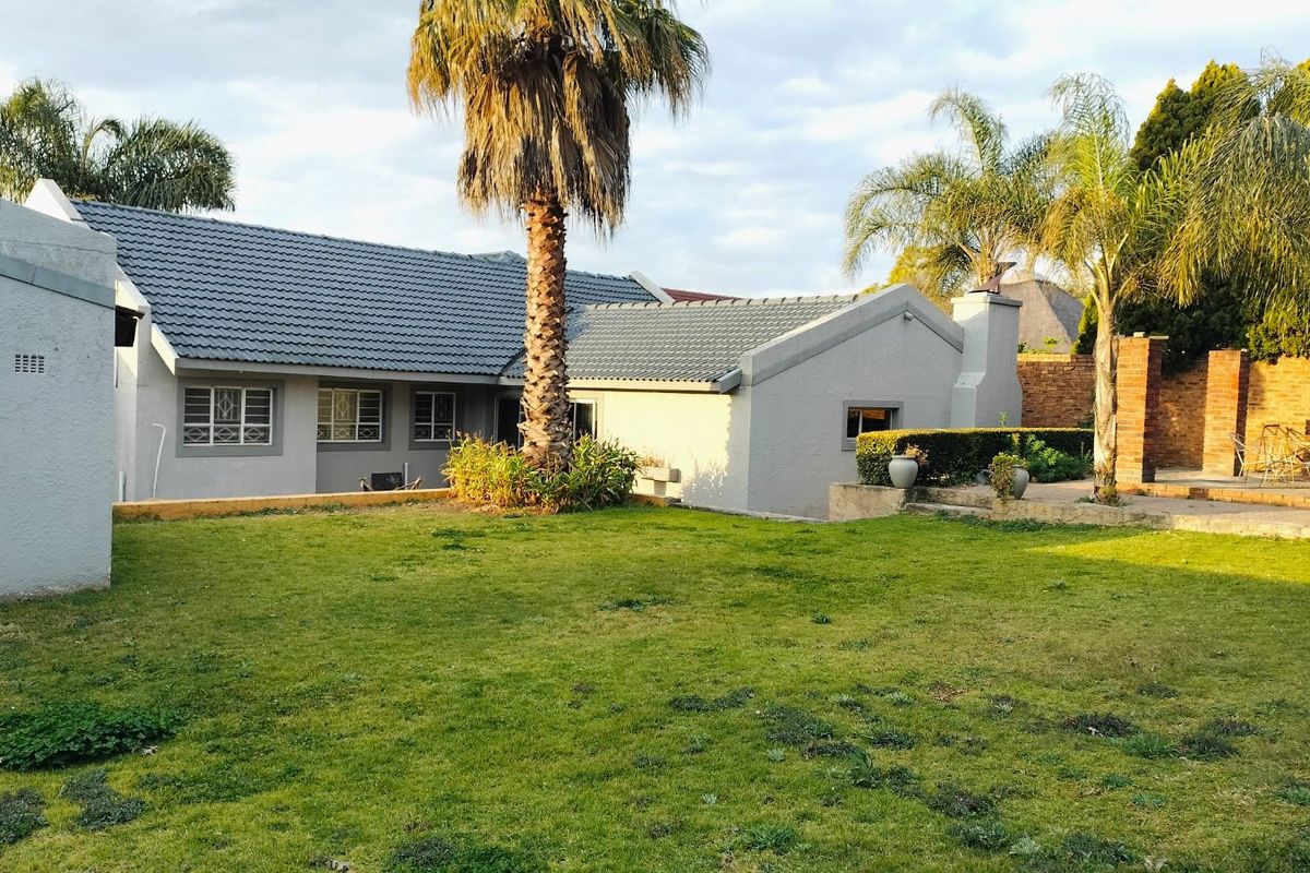 Rear view of the house featuring a tiled roof, grey rendered walls, and a spacious garden area with established palm trees.