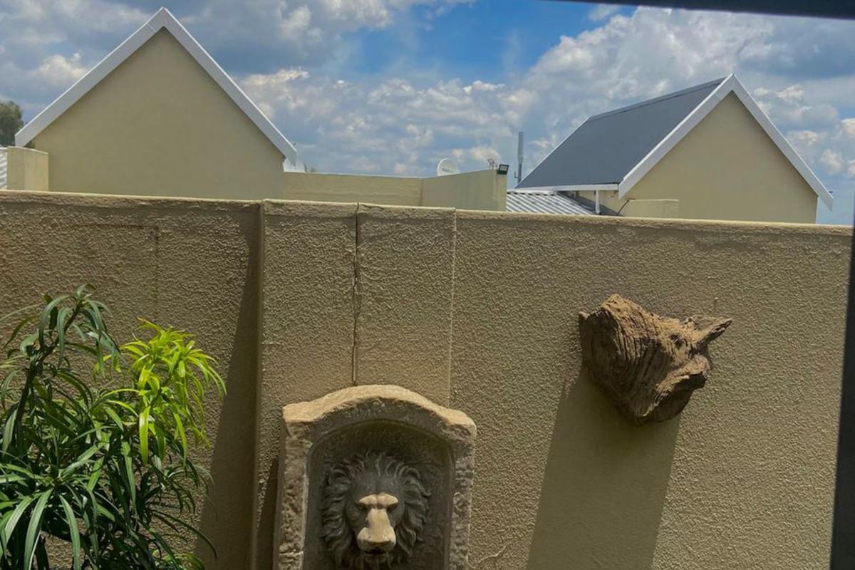 A view of a private courtyard featuring a decorative stone lion wall fountain against a boundary wall with neighbouring townhouse rooflines visible.