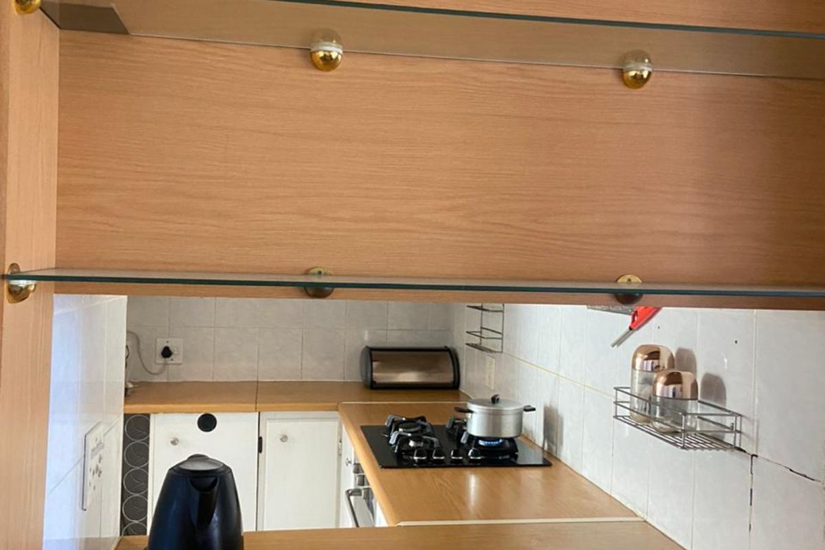 A functional kitchen featuring wooden cabinetry, a built-in gas hob, and glass shelving, providing a practical workspace for daily cooking needs.