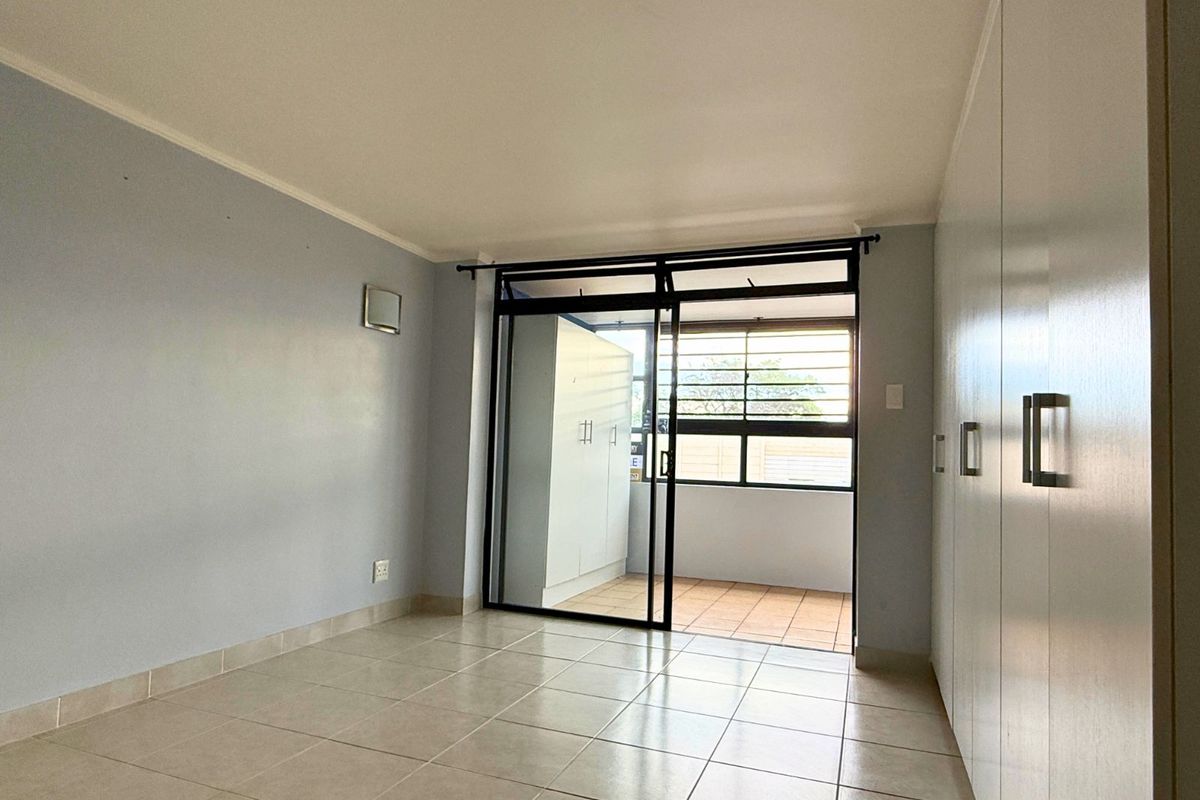 A bright bedroom featuring tiled flooring, built-in cupboards, and a sliding glass door providing access to a private balcony.