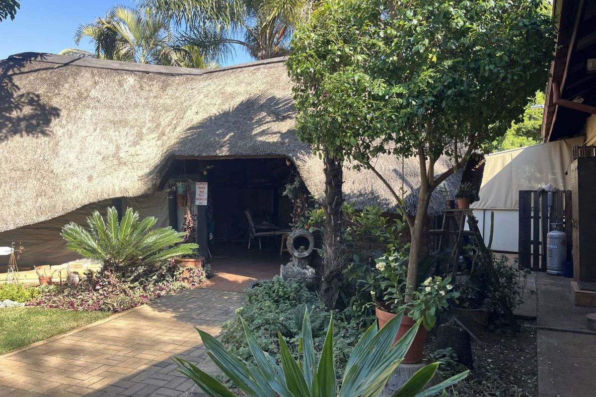 A view of a traditional thatched-roof outdoor entertainment area featuring a paved walkway and established garden surroundings.