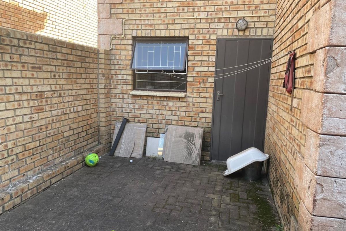 A paved rear courtyard area featuring face-brick walls, a security-barred window, and a solid exterior door.