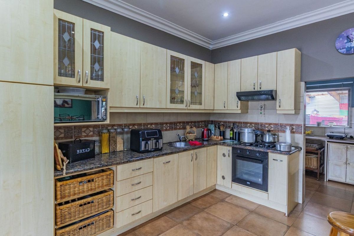 A functional kitchen featuring light wood cabinetry, granite countertops, a built-in oven, gas hob, and extractor fan, with tiled flooring throughout.