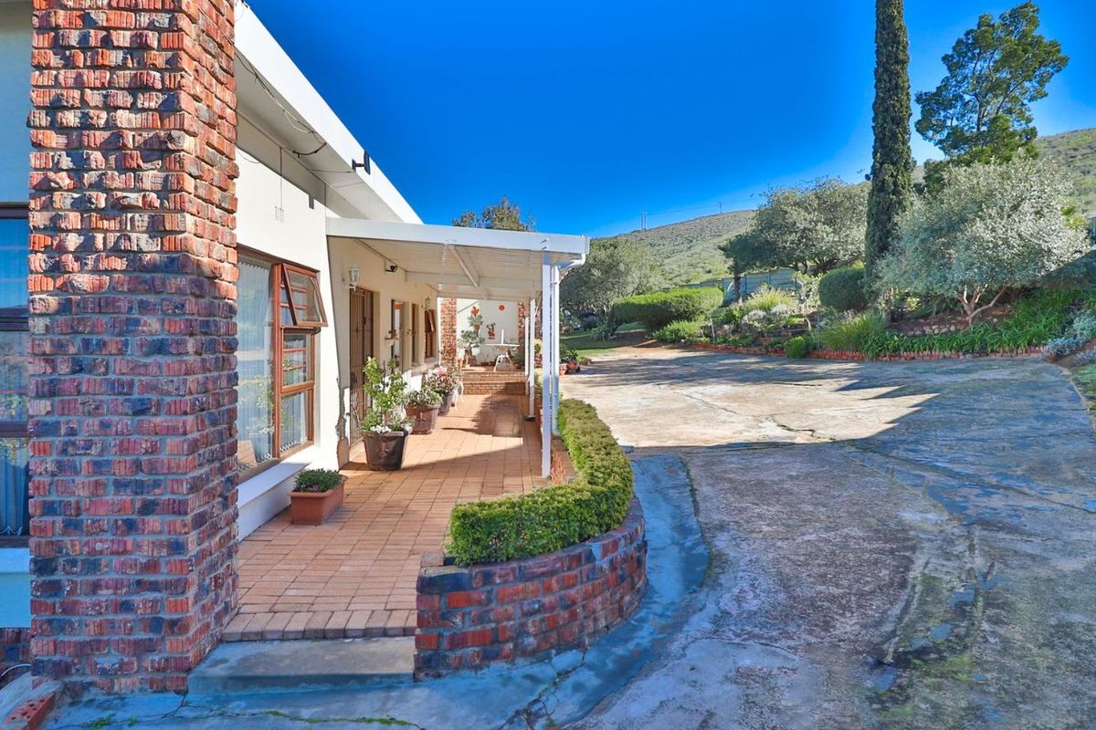 A view of the rear exterior featuring a covered patio with tiled flooring, brick accents, and a large concrete driveway leading to the garden.