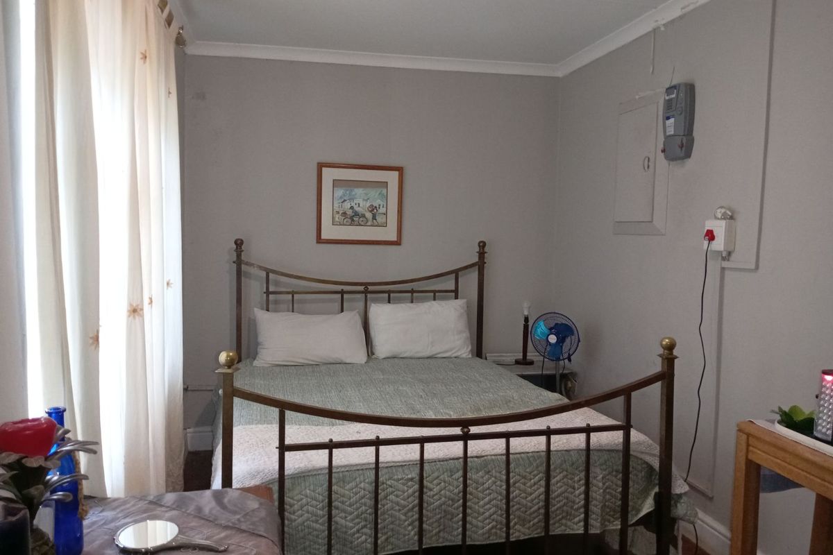 A functional bedroom featuring neutral wall tones, a metal bed frame, and large windows allowing natural light, with visible electrical infrastructure.