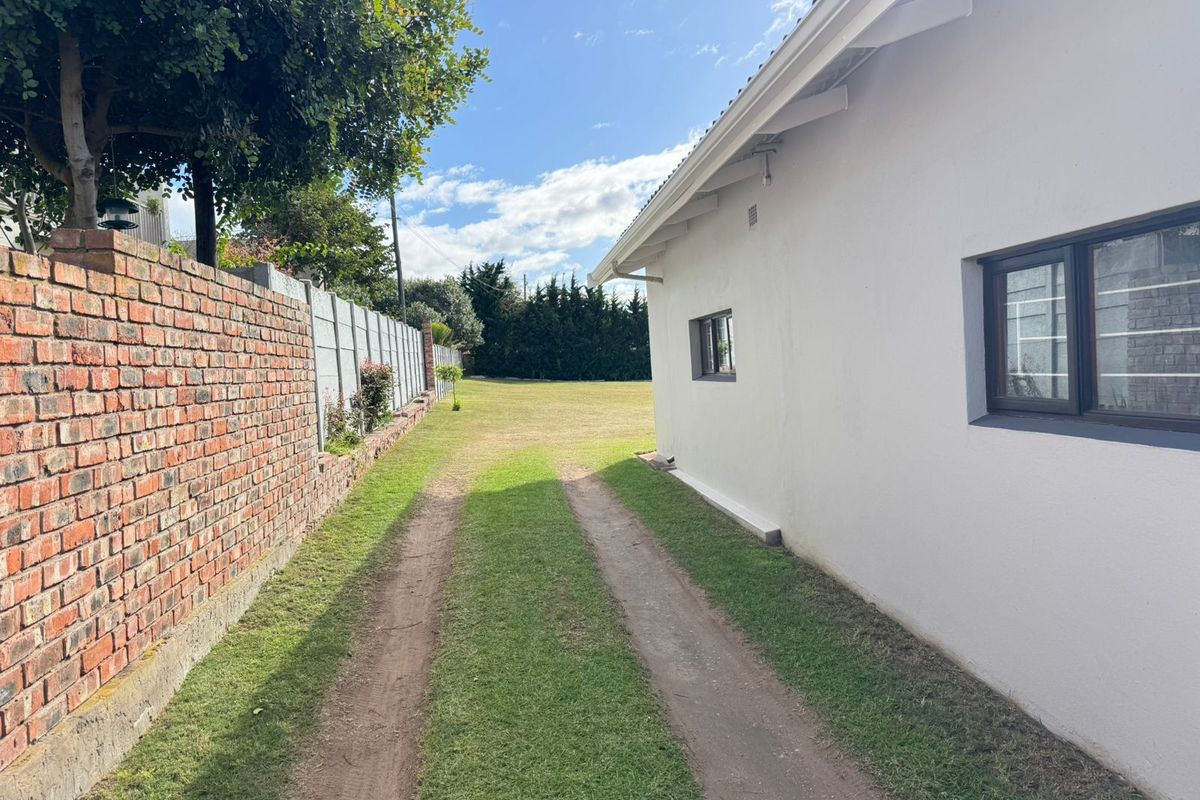 Side view of the property showing a grass driveway, a brick boundary wall, and the side elevation of the residential building.