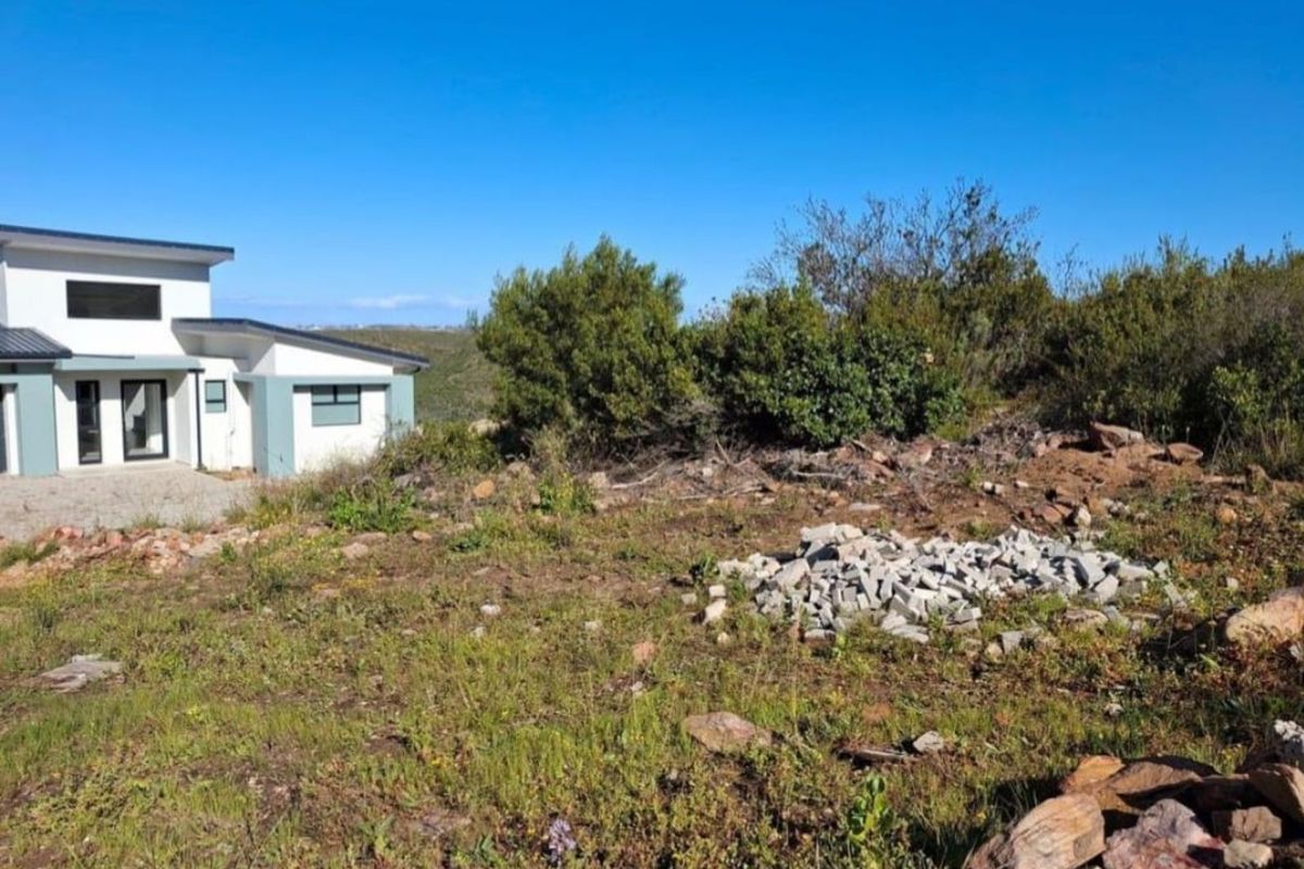 A view of a residential plot featuring natural vegetation and a neighboring modern home, offering potential for development.