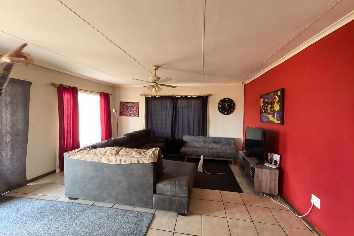 A spacious living room featuring tiled flooring, a ceiling fan, and a bold red accent wall, offering a functional layout for relaxation.