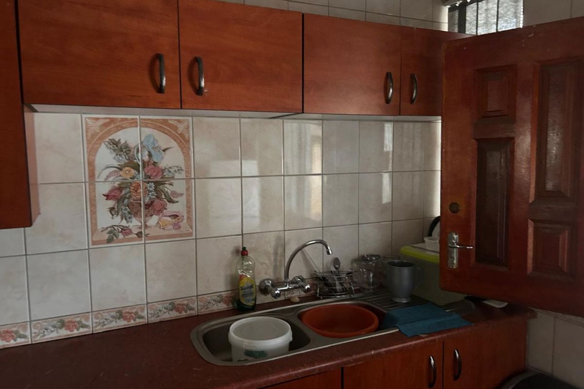 A compact kitchenette featuring wooden cabinetry, a stainless steel double sink, and decorative tiled backsplash.