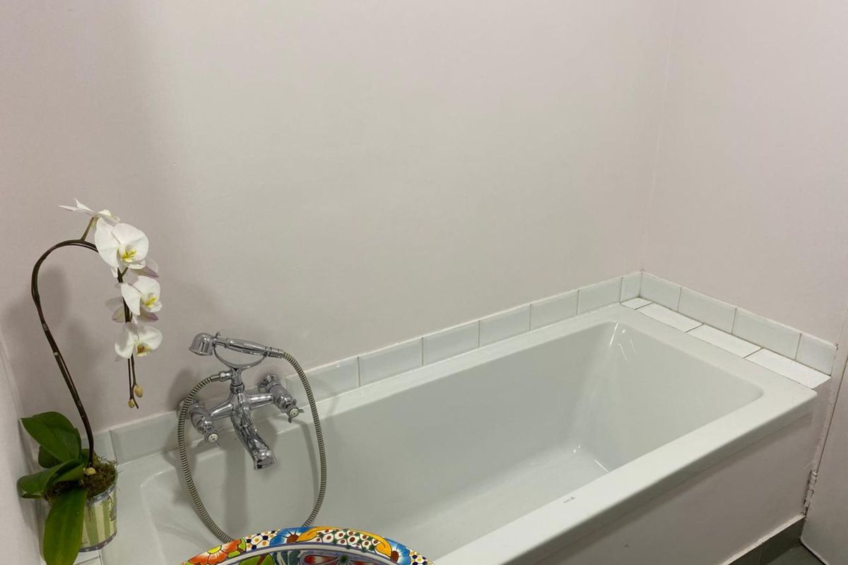 A clean bathroom featuring a standard white bathtub with a chrome mixer tap and handheld shower attachment, finished with simple white wall tiling.
