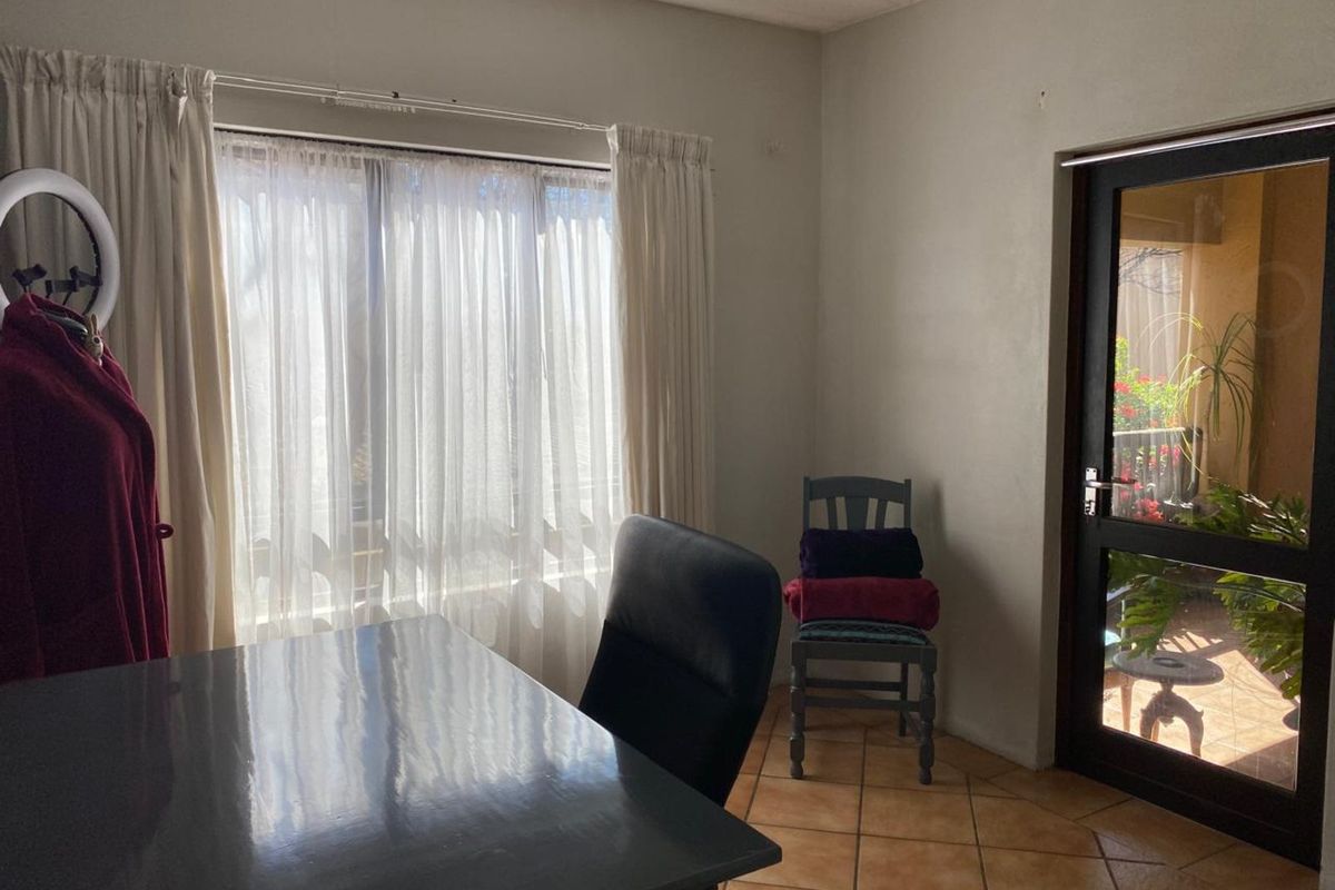 A functional room featuring tiled flooring, large windows with curtains, and a glass-paneled door providing access to an outdoor patio area.