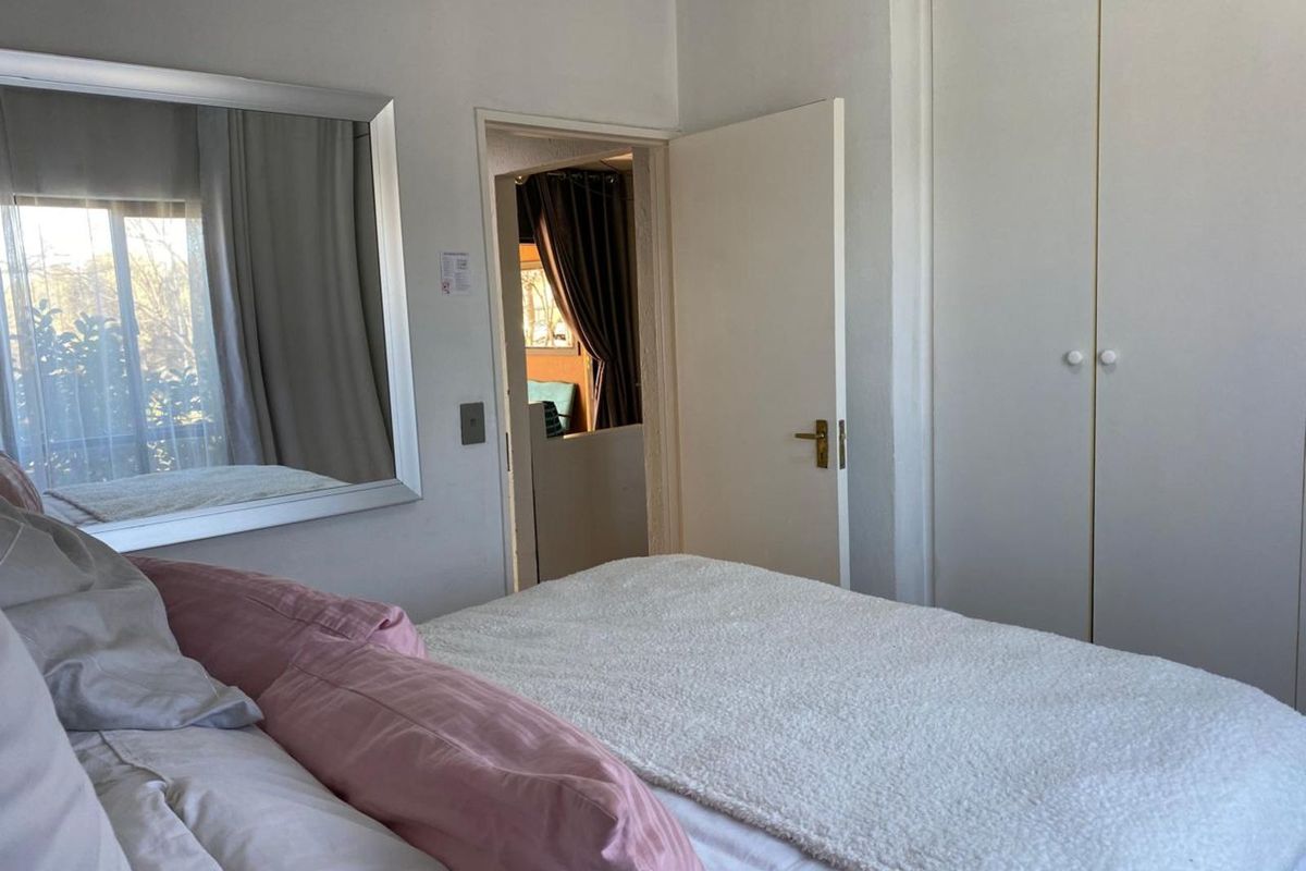 A bedroom featuring built-in cupboards and a doorway leading to an adjacent room, with neutral finishes and natural light.