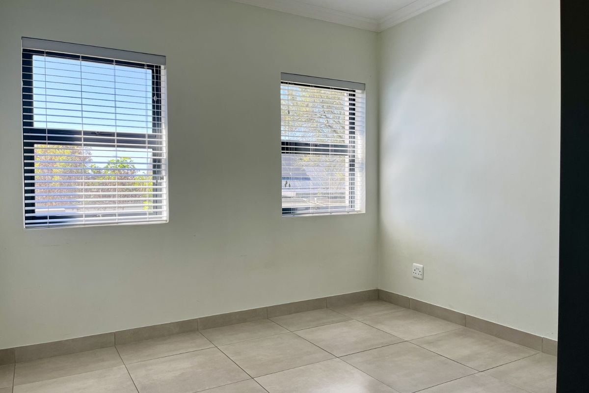 A bright, empty bedroom featuring neutral tiled flooring, clean white walls, and fitted venetian blinds on the windows.