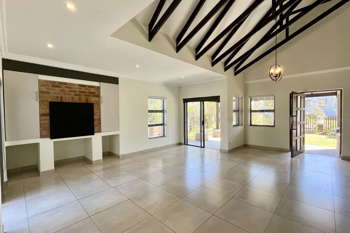Spacious living area featuring high vaulted ceilings with exposed timber beams, tiled flooring, and a built-in brick feature wall with integrated shelving.
