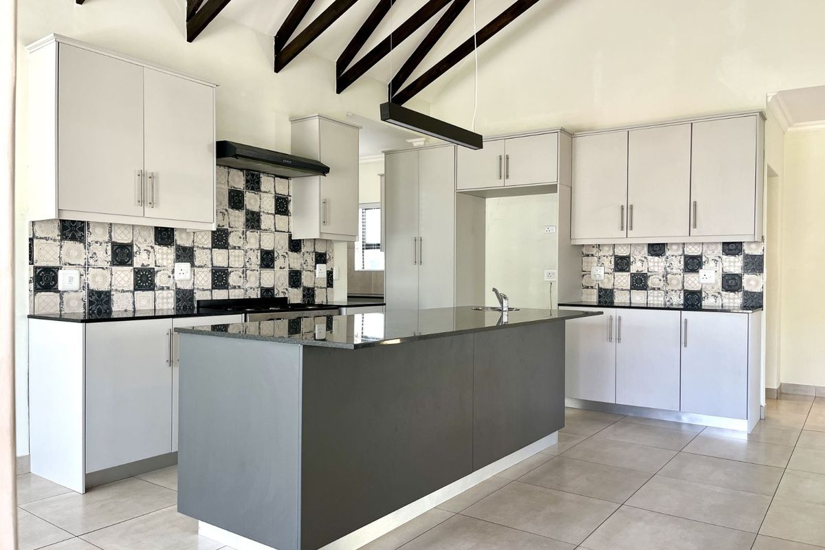 Modern kitchen featuring a central island, stone countertops, patterned tile backsplash, and high vaulted ceilings with exposed timber beams.