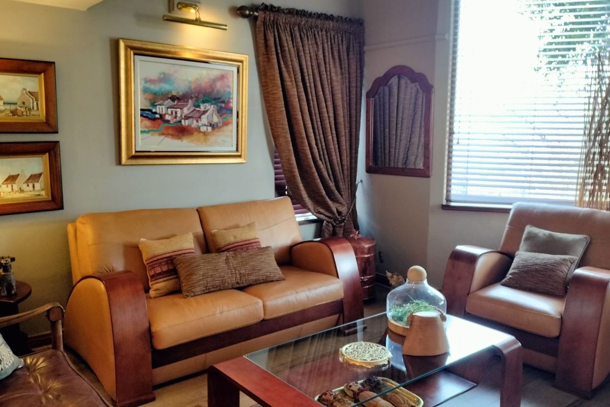 A cozy living room featuring neutral wall tones, large windows with blinds, and classic architectural detailing.